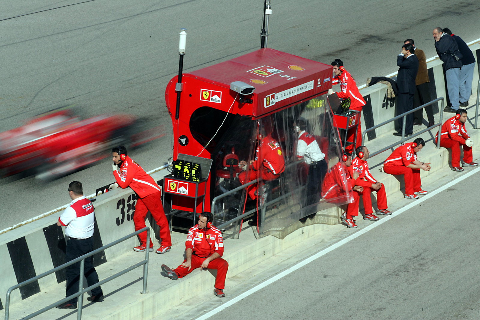 The Ferrari team relax on the pit wall as Rubens Barrichello drives past